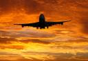 A plane flying in front of a sunset (Canva)